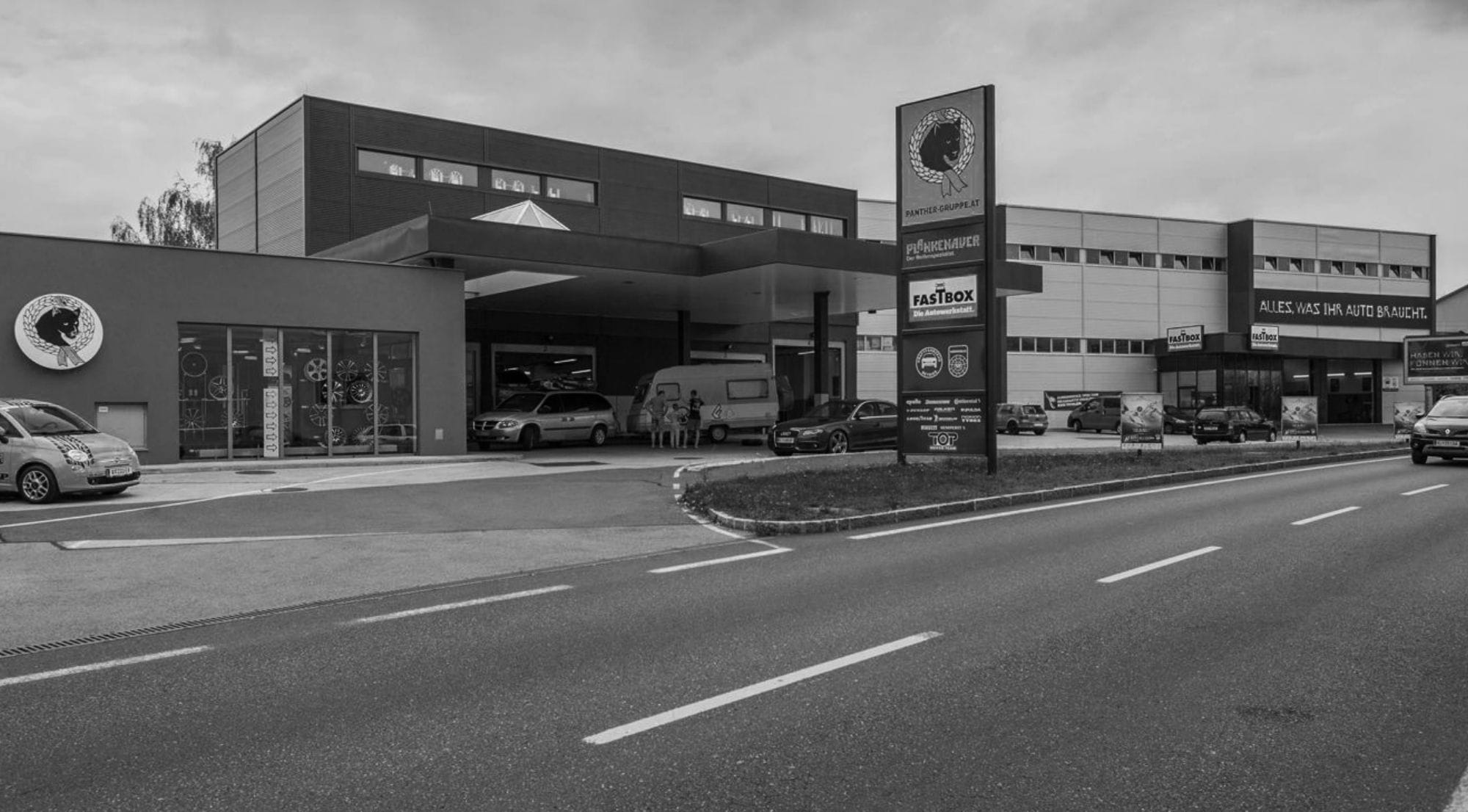 Fassade eines Plankenauer-Gebäudes mit mehreren Fahrzeugen davor – moderner Firmenstandort mit großflächiger Beschilderung.