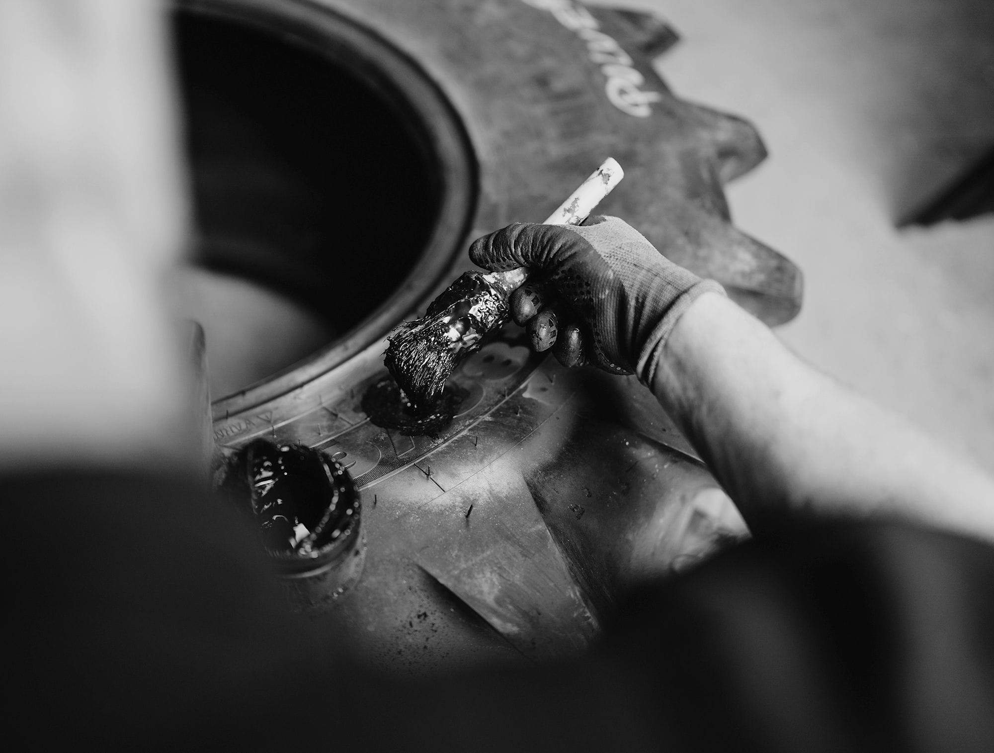 Ein Mechaniker trägt mit einem Pinsel eine klebrige Gummilösung auf einen Traktorreifen auf, um ihn auf die Reparatur vorzubereiten.