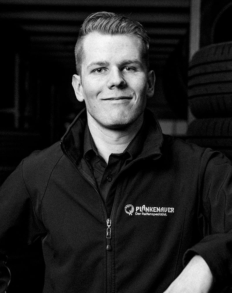 Nahaufnahme eines lächelnden Mitarbeiters in schwarzer Arbeitskleidung mit Firmenlogo.